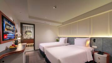 A hotel room with two beds, a TV, a desk with fruit, a mirror, and a nightstand with a phone.