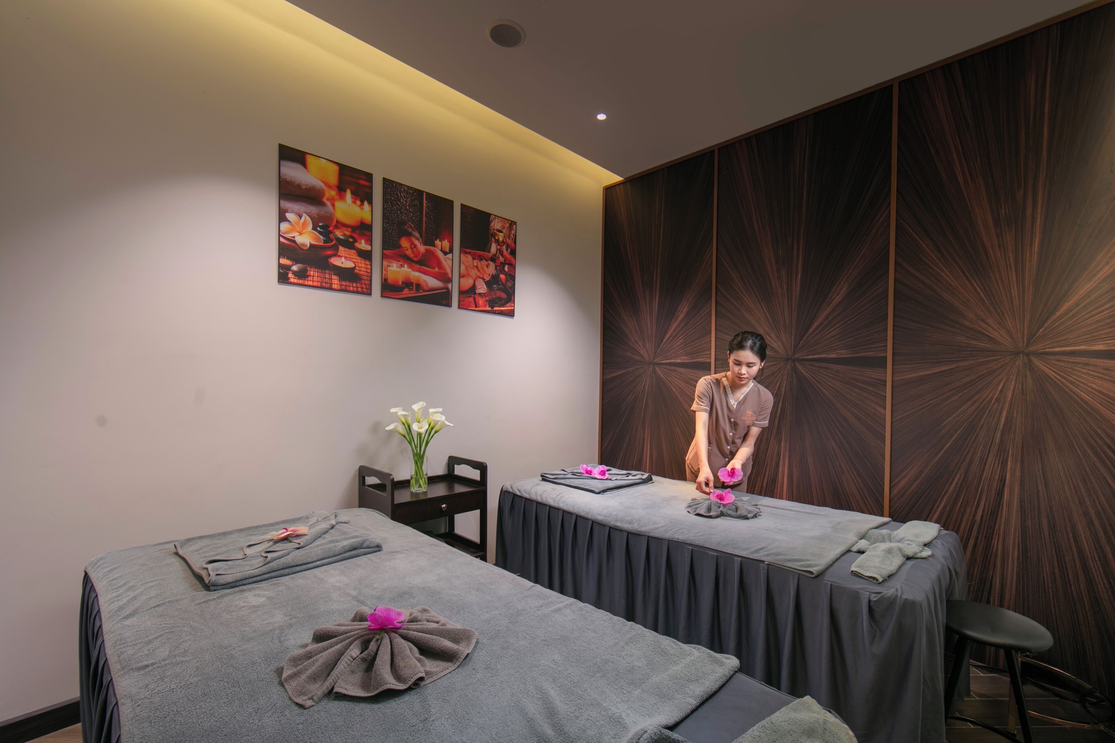 Un cuarto de spa con dos camillas de masaje, una pared con diseño radial y una persona atendiendo a un cliente.