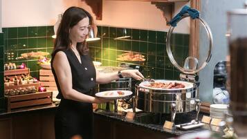 A buffet setup with a variety of food items, a person serving food, and a decorative towel ring.