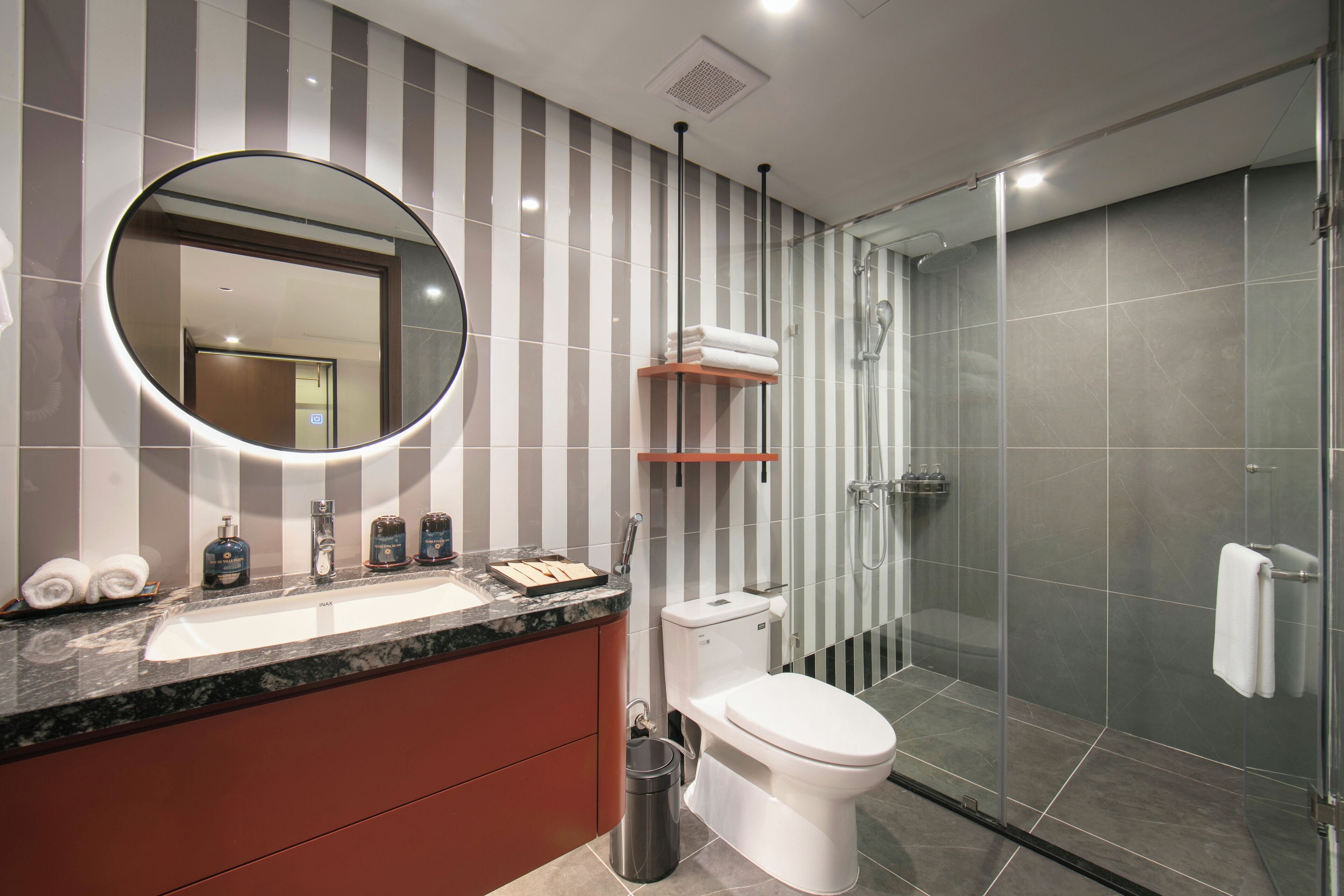 Un baño moderno con lavamanos de mármol, inodoro, ducha con cerramiento de vidrio y diseño de pared a rayas.