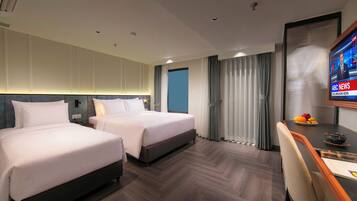 Ein Hotelzimmer mit zwei Betten, einem Schreibtisch mit Stuhl, einem Fernseher und einem Fenster mit Vorhängen.