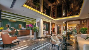 Un hall de hotel con mostrador de recepción, zona de estar y una escalera que sube a un nivel superior.