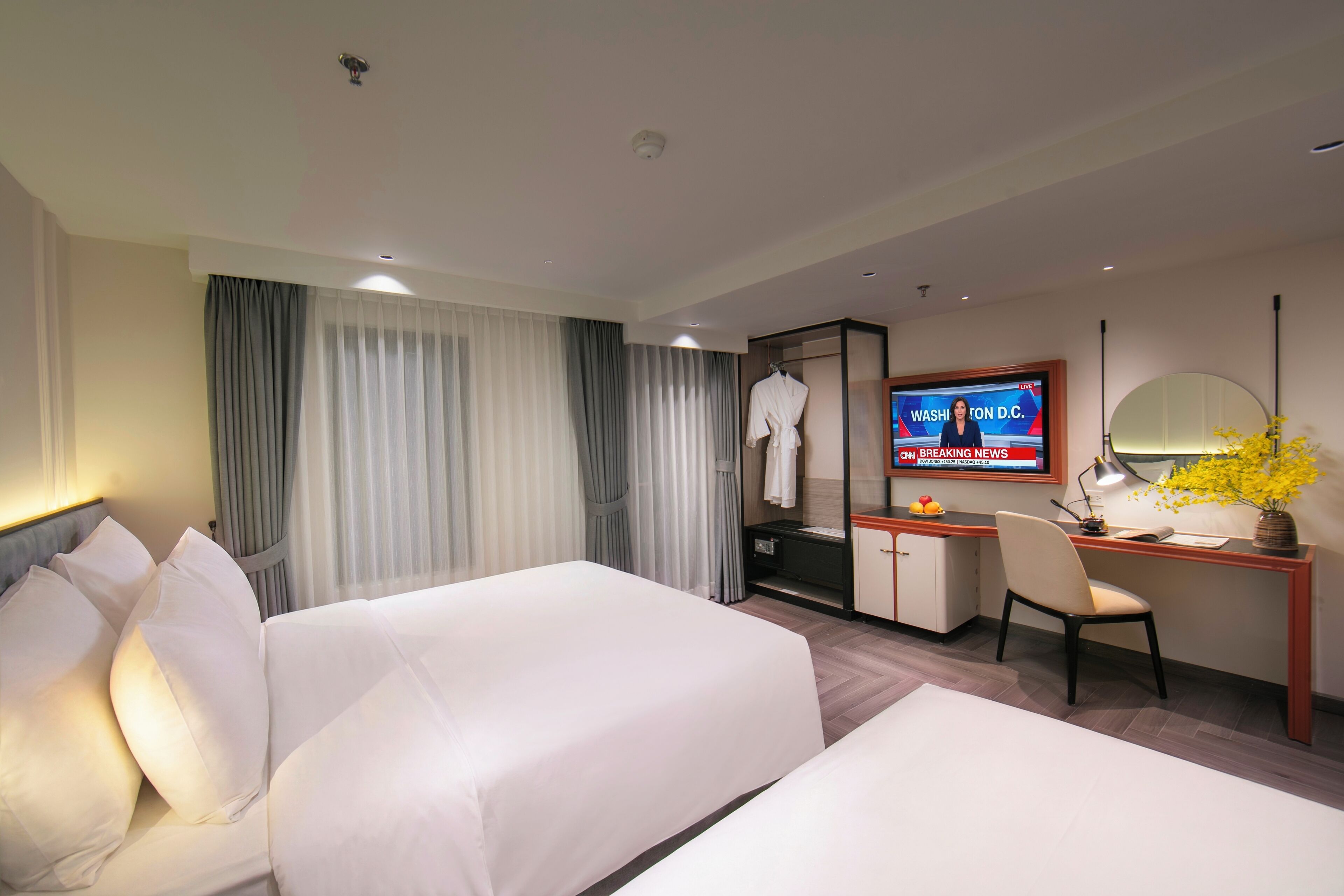 Ein Hotelzimmer mit zwei Betten, einem Schreibtisch, einem Fernseher, der Nachrichten zeigt, und einem Spiegel.