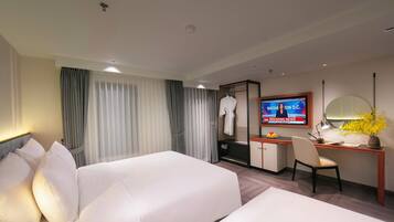 Ein Hotelzimmer mit zwei Betten, einem Schreibtisch, einem Fernseher, der Nachrichten zeigt, und einem Spiegel.