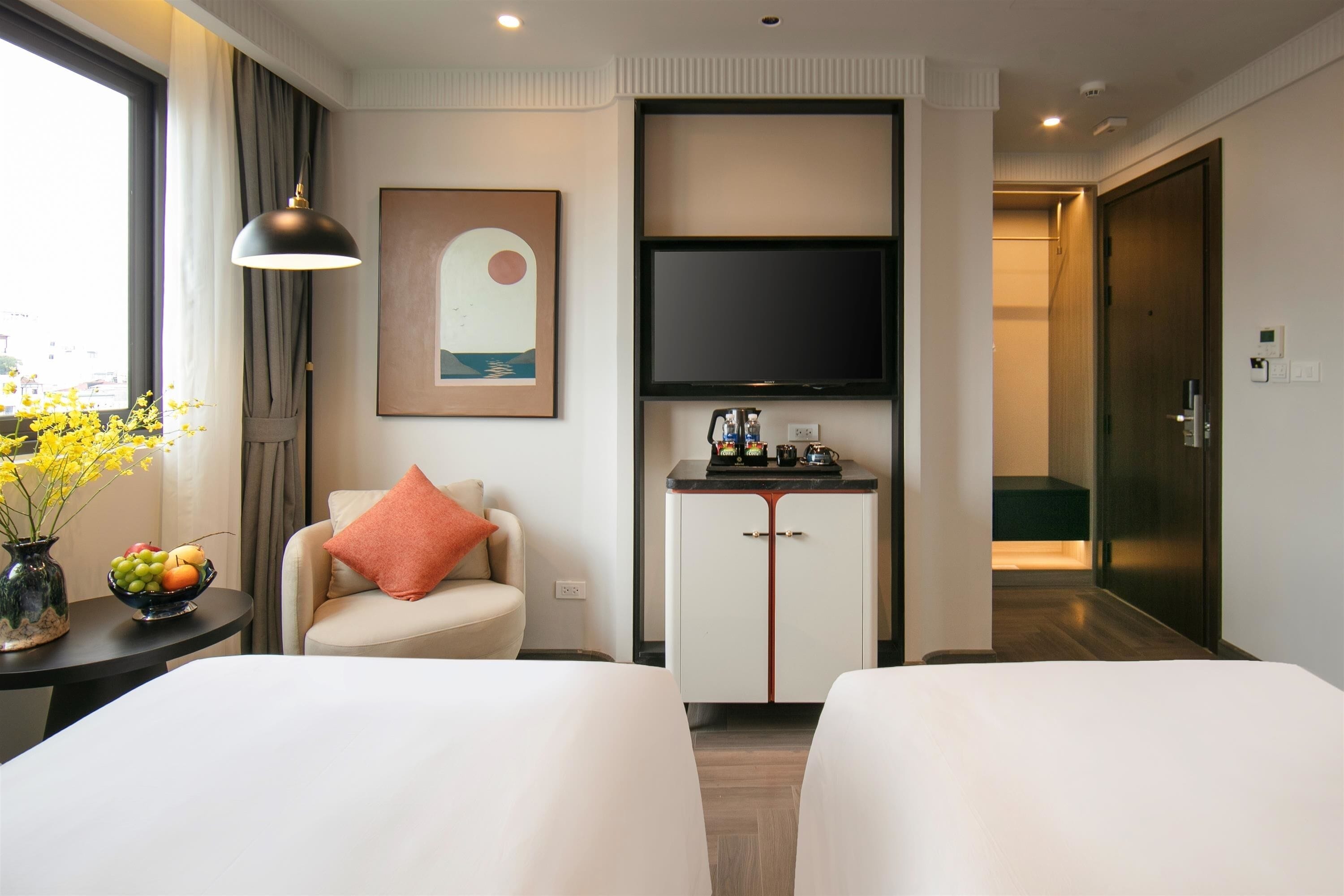 Habitación de hotel con dos camas, un escritorio con un jarrón de flores, un televisor de pantalla plana, un cuadro y vistas a la ciudad.