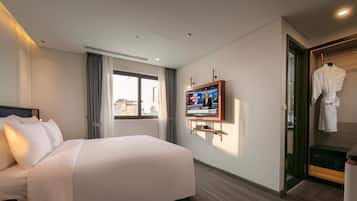 Une chambre d’hôtel avec un grand lit, un téléviseur fixé au mur, un peignoir suspendu à un porte-manteau et une vue sur la ville par la fenêtre.