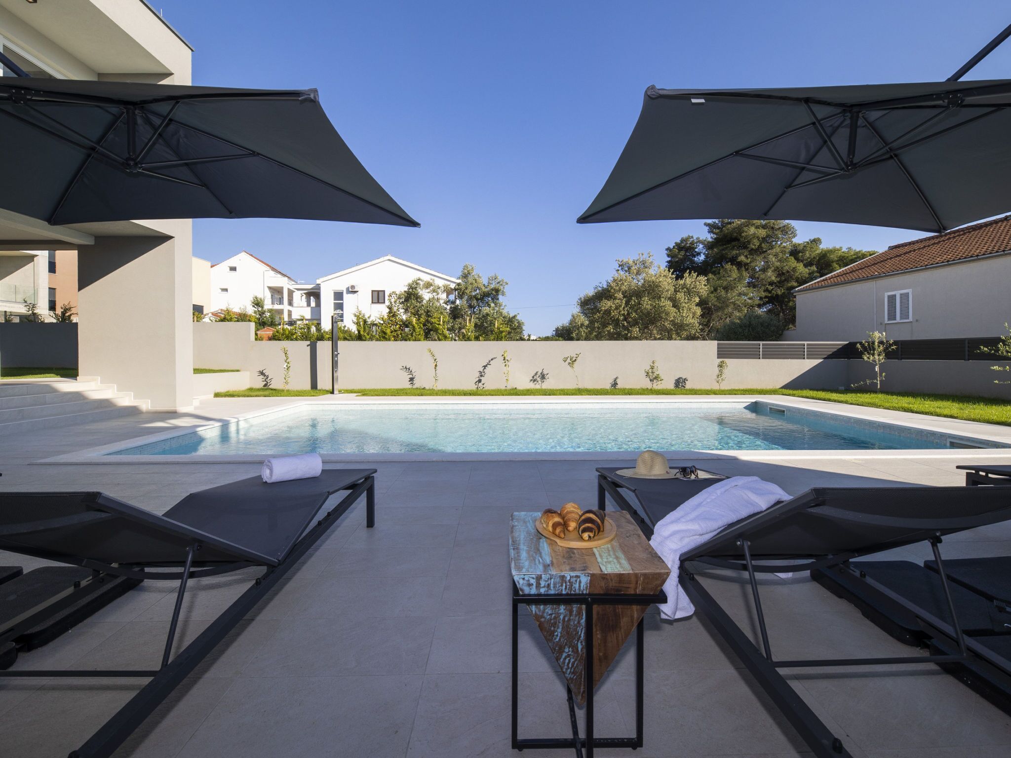 A poolside area with lounge chairs, umbrellas, and a table with pastries.