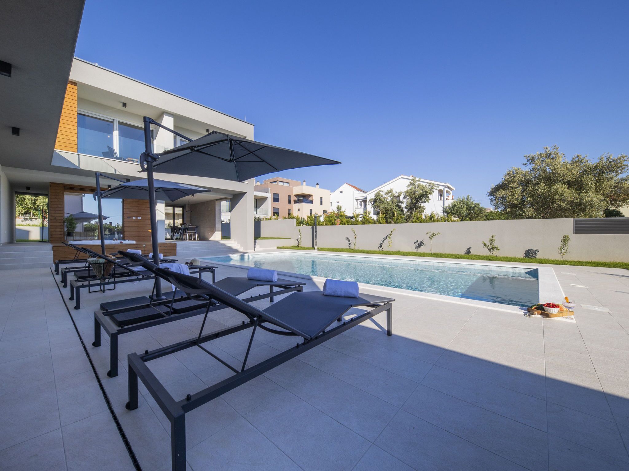 A modern outdoor pool area with sun loungers and umbrellas, surrounded by a residential building.