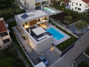 Et moderne hus med to etager, en swimmingpool, solpaneler og en bil foran.