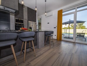 Eine moderne Küche mit Bar, Edelstahlgeräten und einem großen Schiebeglasfenster zum Außenpool.