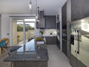 Una cocina moderna con una isla central, electrodomésticos de acero inoxidable y un ventanal corredero que da a un espacio exterior.