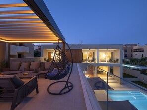Et moderne udendørs opholdsområde med hængestol, sofaer og swimmingpool.
