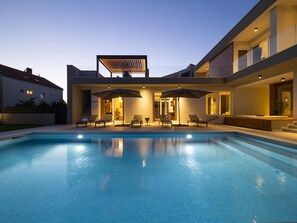 Et moderne hus med swimmingpool, udendørs møbler og en overdækket patio.