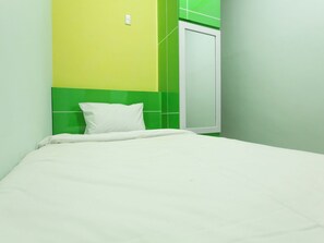 A single bed with a white mattress and pillow in a room with green and yellow walls. - Reddoorz Syariah @ Dinda Residence (Medan)