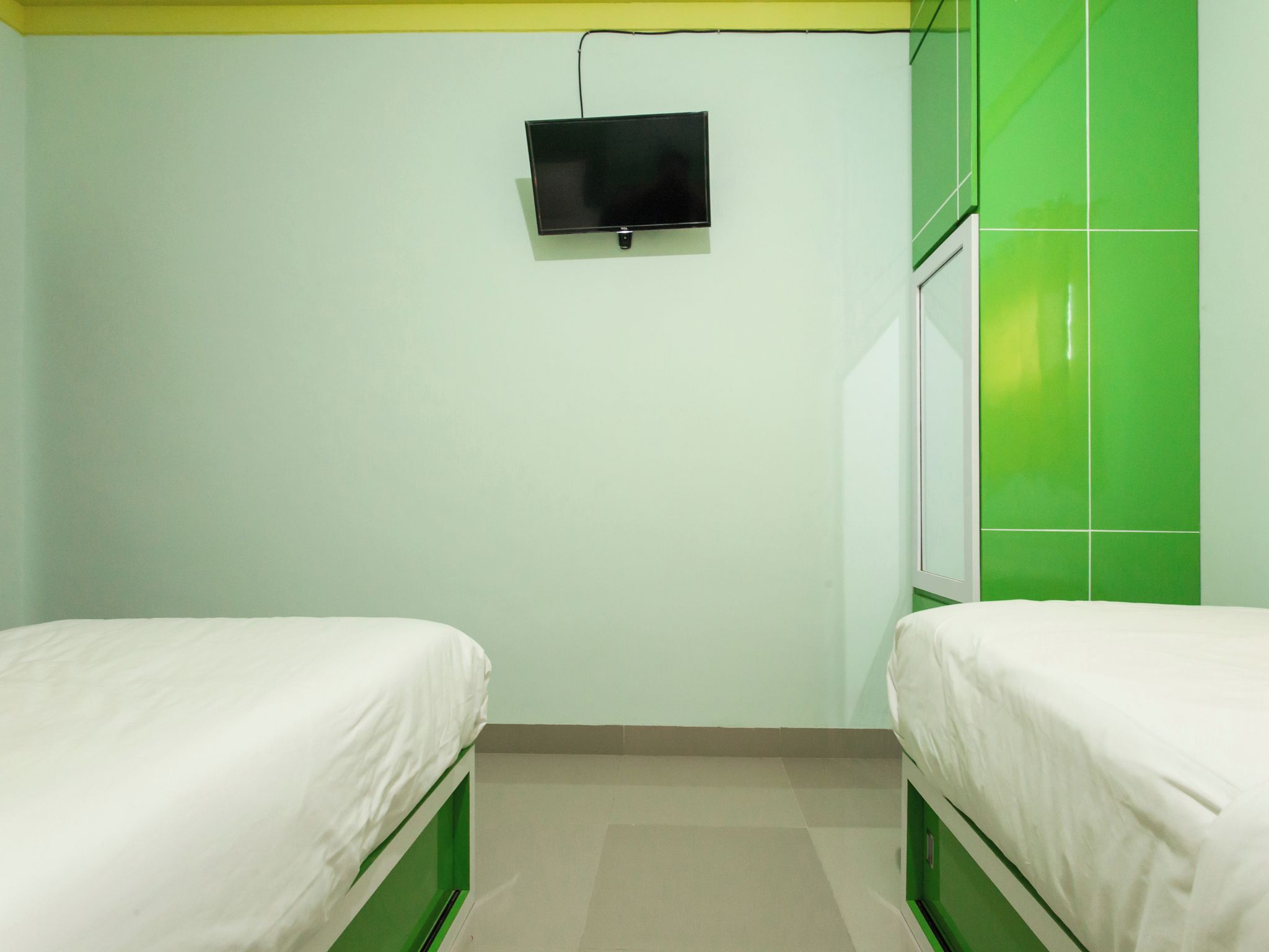 Une chambre avec deux lits, un téléviseur fixé au mur et des murs verts et blancs.