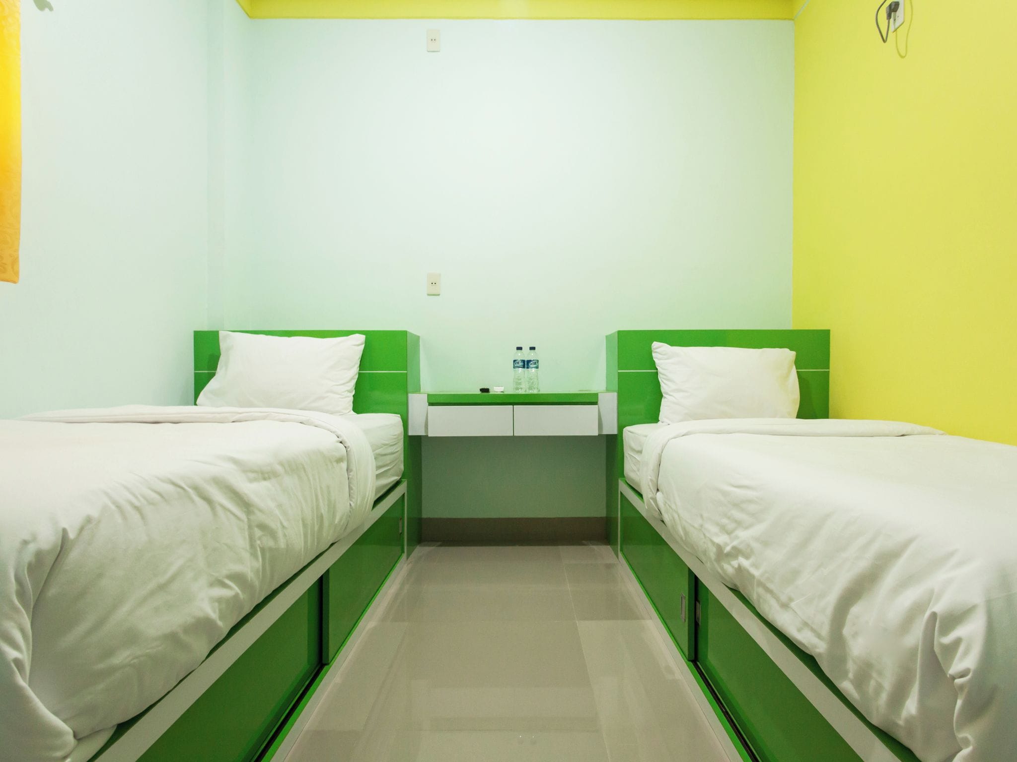 A room with two beds, a small table, and a wall-mounted outlet.