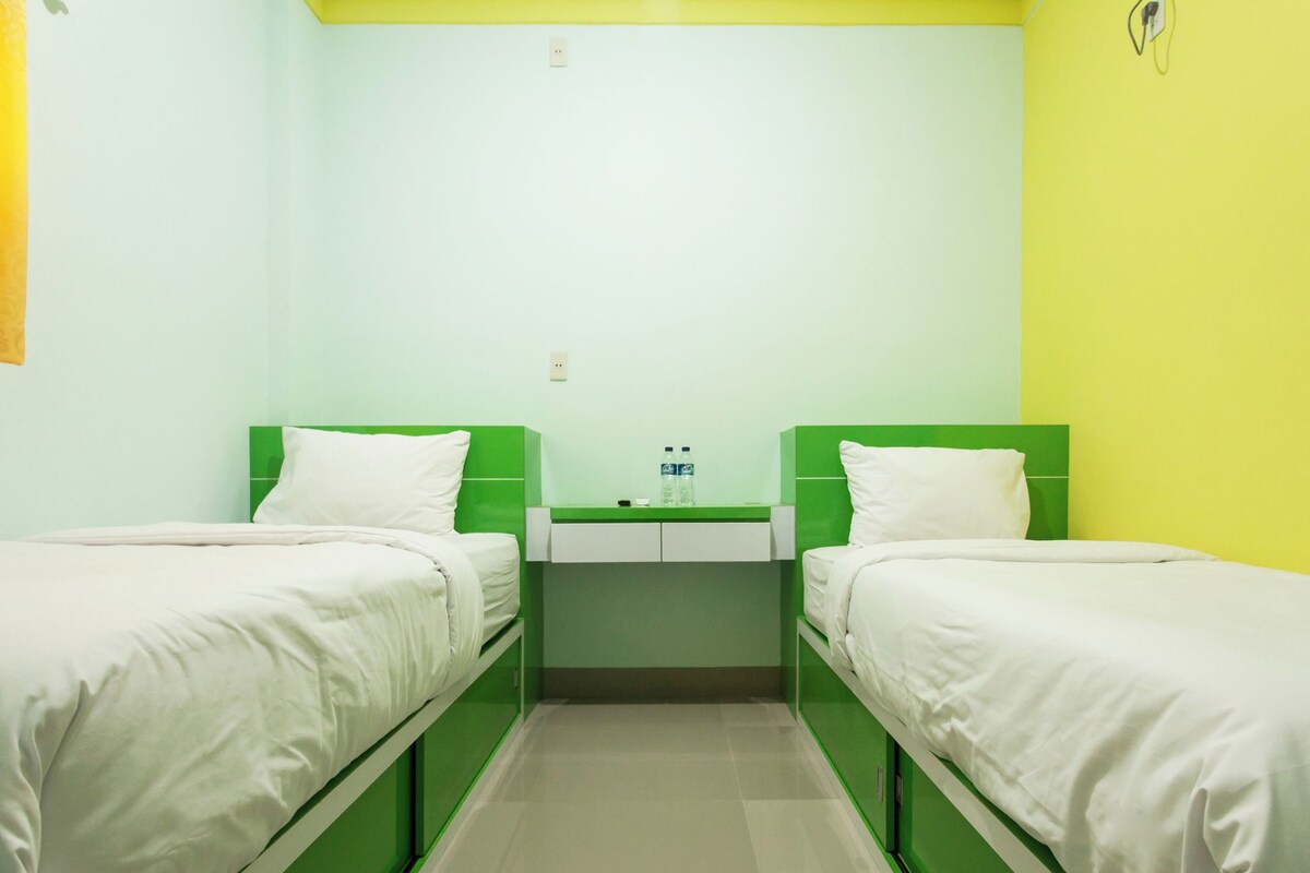A room with two beds, a small table, and a wall-mounted outlet.