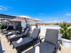 A rooftop terrace with lounge chairs, umbrellas, a bar area, and a potted plant. - Rooftop heated pool Villa Jelena by Interhome (Crno)
