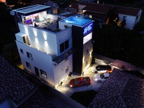 A modern two-story building with a rooftop terrace and a sign indicating a hotel. There are three cars parked in front. - Rooftop heated pool Villa Jelena by Interhome (Crno)