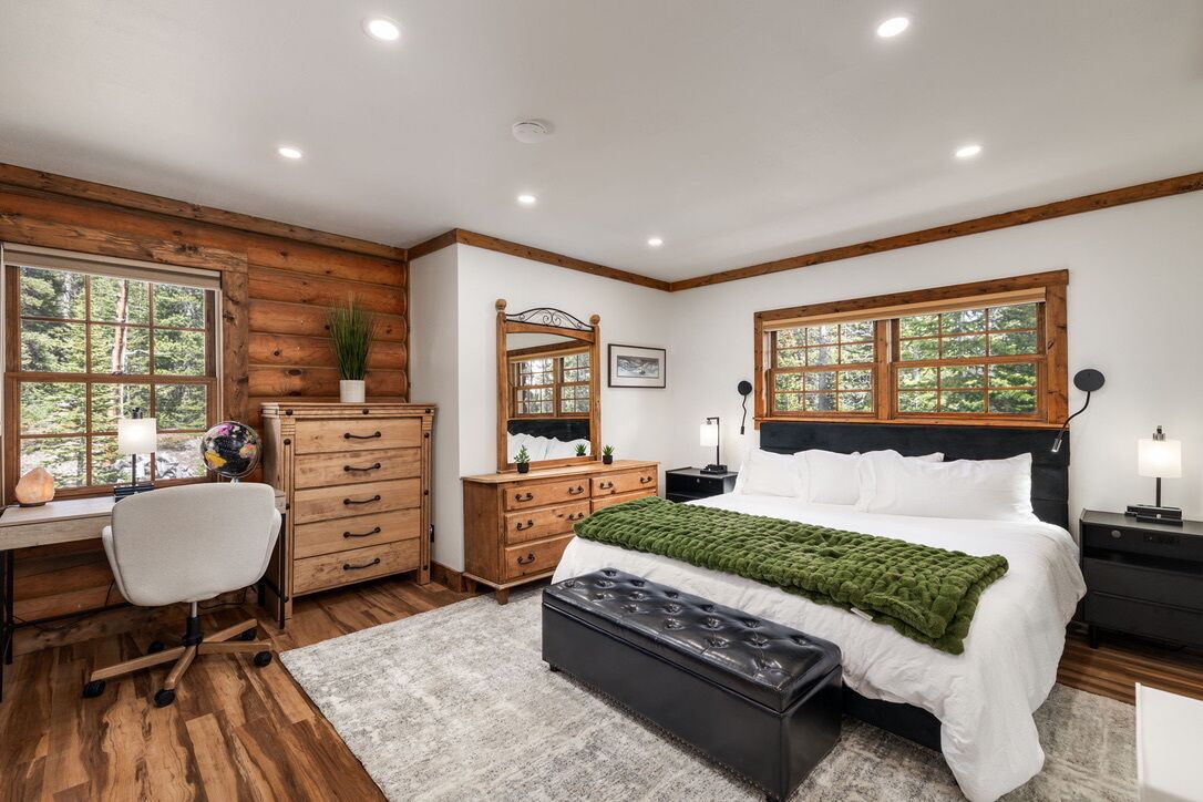A bedroom with a wooden desk, a bed with a green blanket, a dresser, and a nightstand.