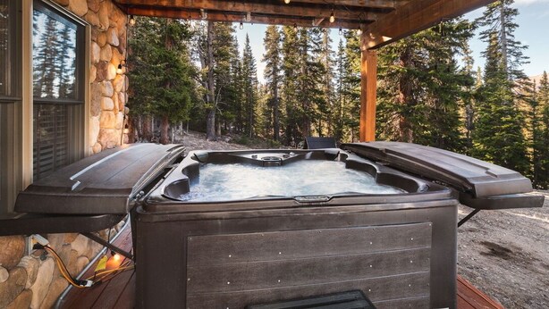 A hot tub under a wooden pergola with a stone wall backdrop and a forest view. - Newly Remodeled Gemini Terrace w/Hot Tub (Fairplay)