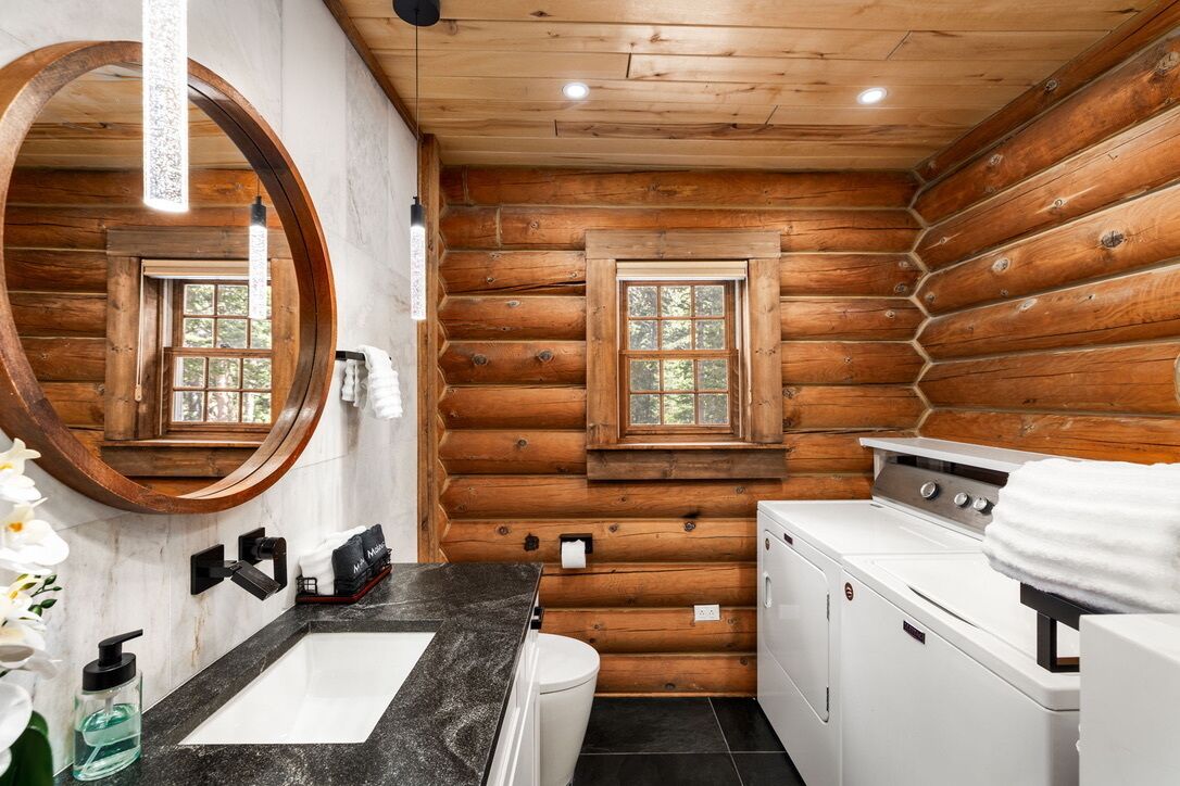 A log cabin bathroom with a sink, mirror, window, and washing machine.