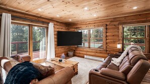 A log cabin interior with a wooden ceiling, large windows, a flat-screen TV, a sofa, and a fireplace. - Newly Remodeled Gemini Terrace w/Hot Tub (Fairplay)