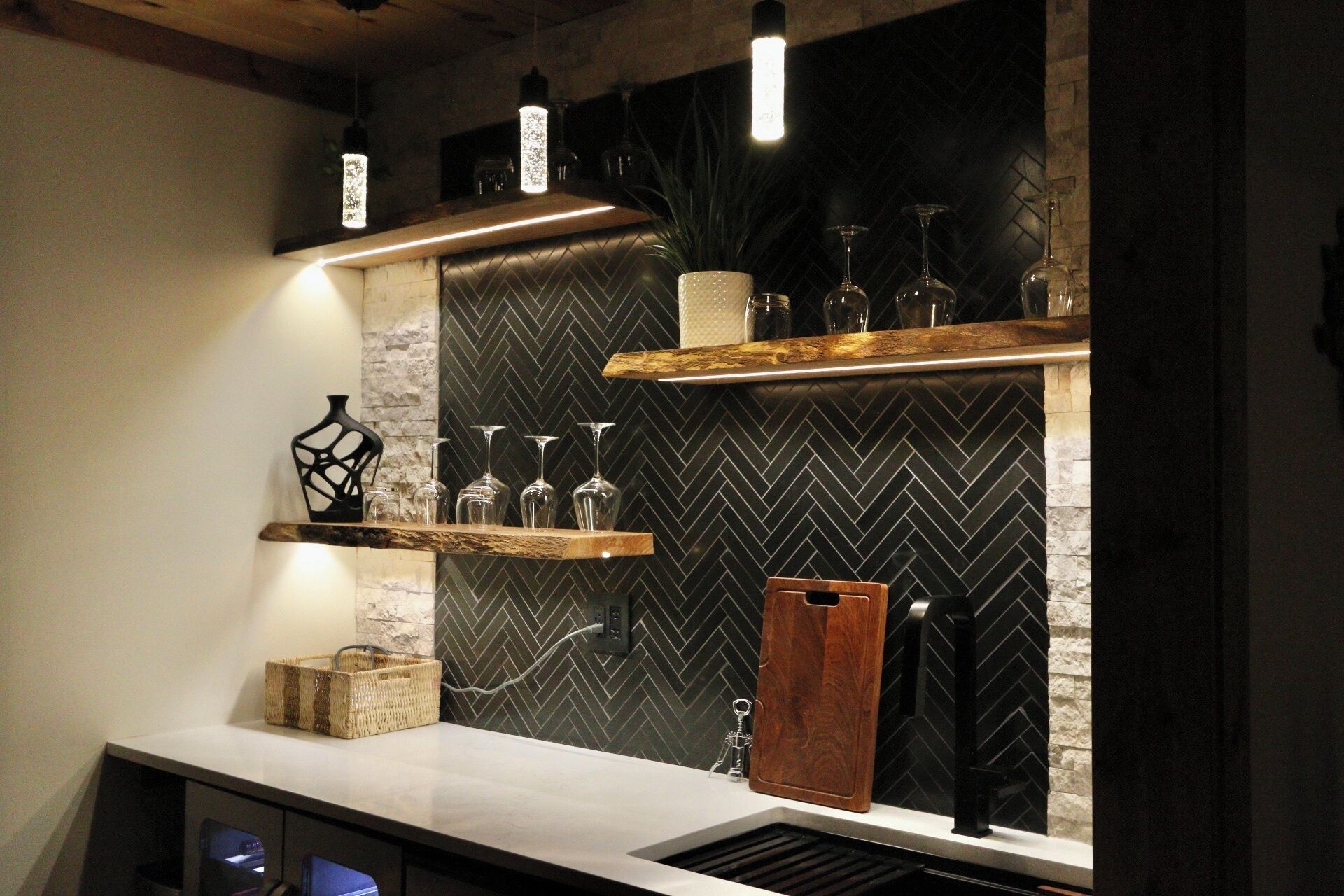 Una cocina con salpicadero de diseño en tablero de ajedrez, estantes de madera y lámparas colgantes.