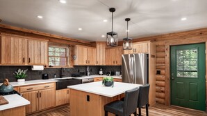 A modern kitchen with wooden cabinets, a central island, stainless steel appliances, and a green door. - Newly Remodeled Gemini Terrace w/Hot Tub (Fairplay)