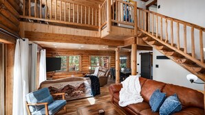 A log cabin interior with a wooden staircase, a living room with a brown leather sofa, a blue armchair, and a fireplace. - Newly Remodeled Gemini Terrace w/Hot Tub (Fairplay)