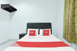 Una cama con cabecera negra, dos almohadas rojas, una colcha blanca y un plaid rojo y blanco.