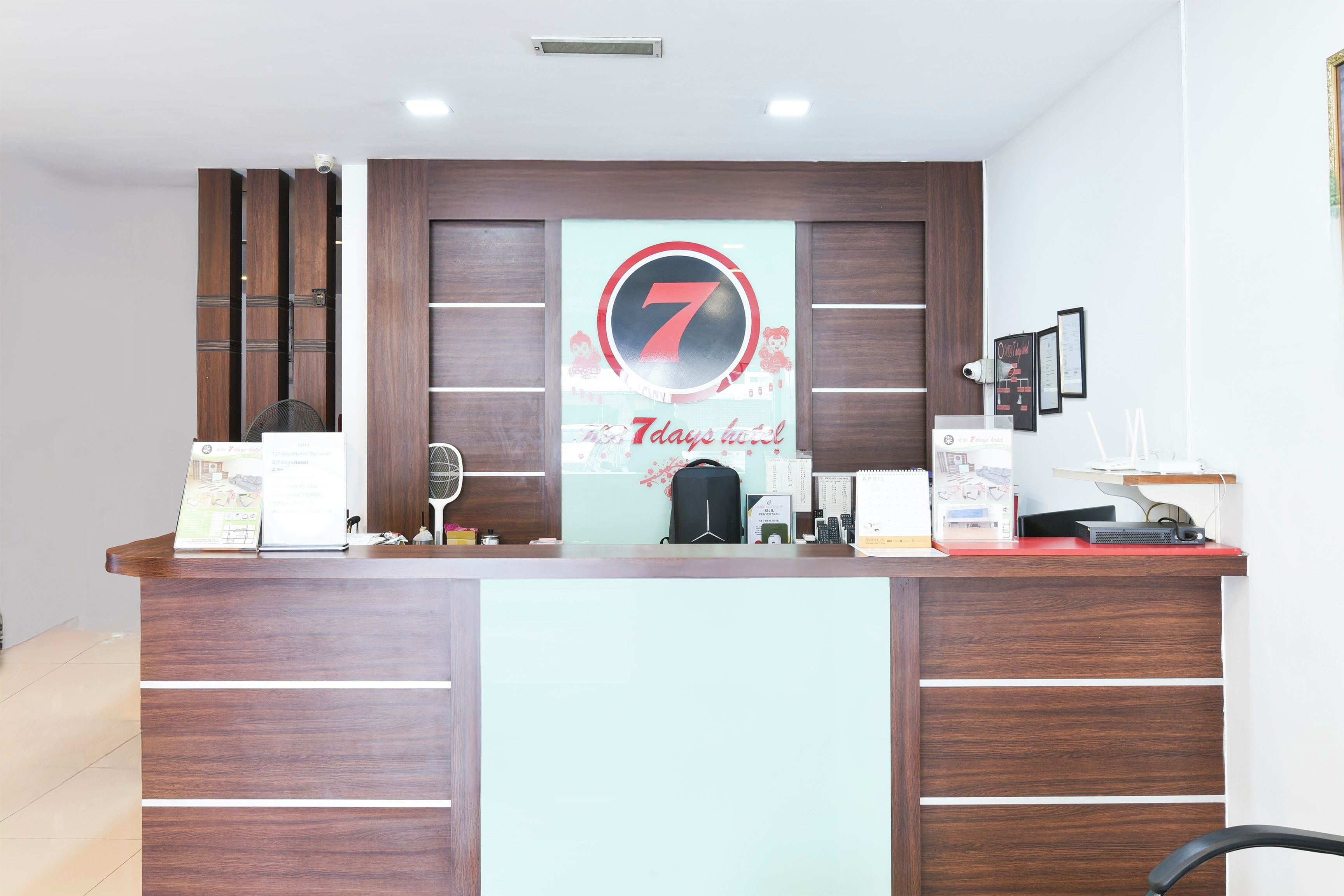 A reception desk with a prominent number 7 sign, a fan, a black bag, and various items on the counter.