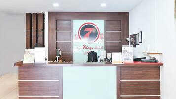A reception desk with a prominent number 7 sign, a fan, a black bag, and various items on the counter.