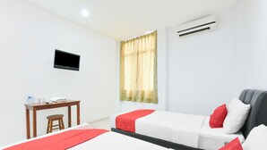 A hotel room with two beds, a desk, a chair, a TV, and an air conditioning unit.