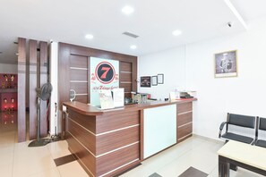 Mostrador de recepción de hotel con un cartel que indica que es un hotel de 7 días, un ventilador, una barra y una zona de estar.