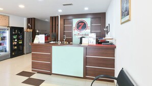A hotel reception desk with a '7' logo, a refrigerator, and a counter with various items.