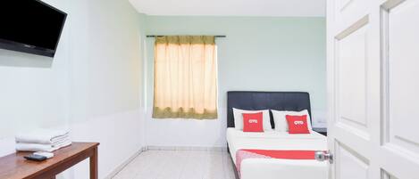 Habitación de hotel con cama, televisor montado en la pared, una mesa con silla y ventana con cortinas.