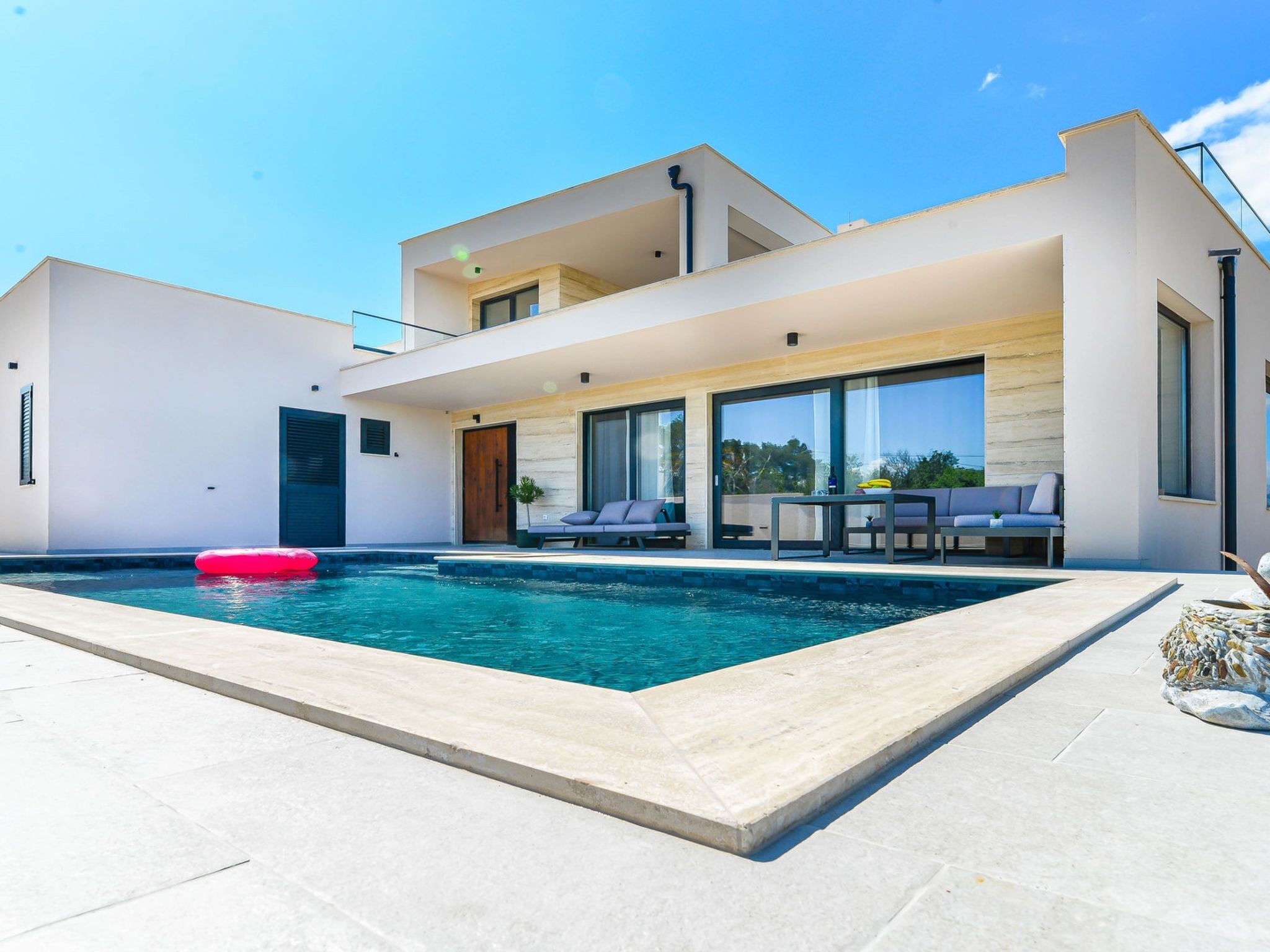 A modern two-story house with a swimming pool, outdoor seating, and large windows.