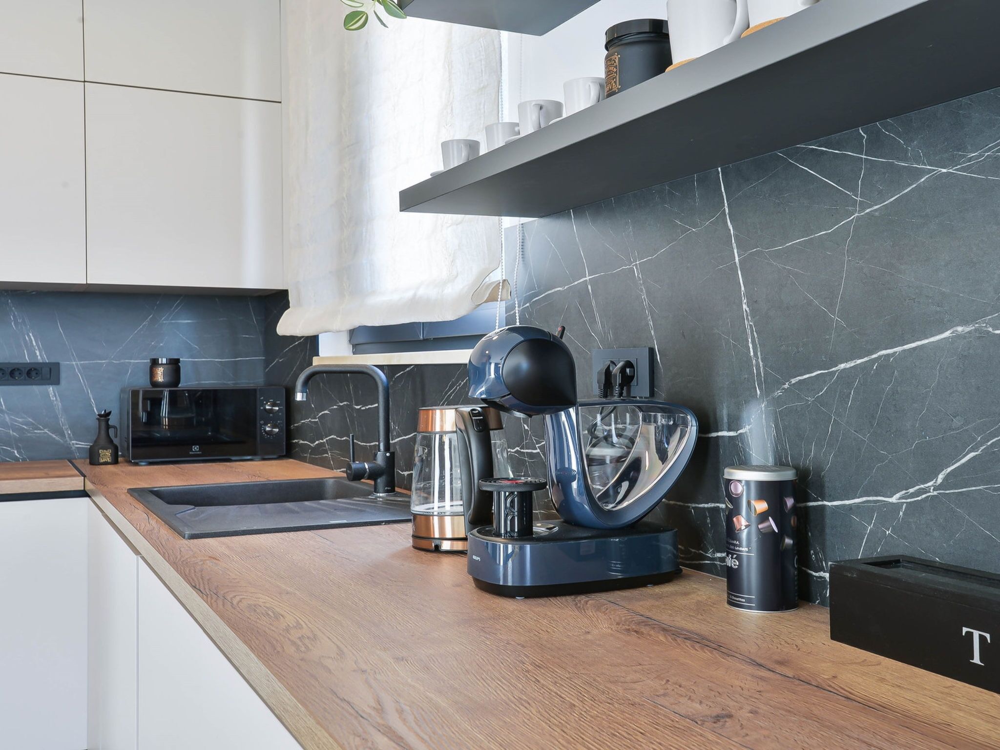 A modern kitchen with a marble backsplash, a coffee machine, a kettle, and a coffee maker on the counter.