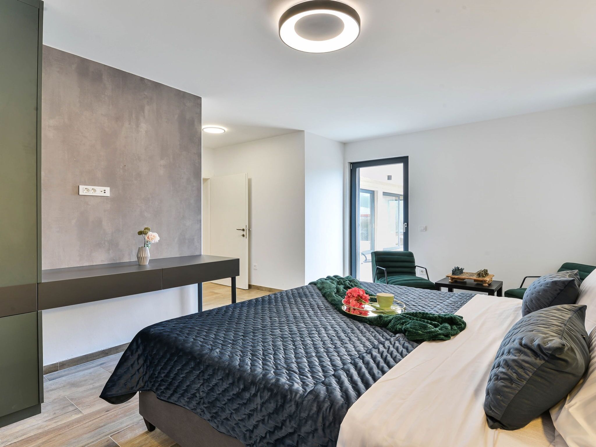 Ein modernes Schlafzimmer mit Bett, Nachttisch und Blick ins Freie.
