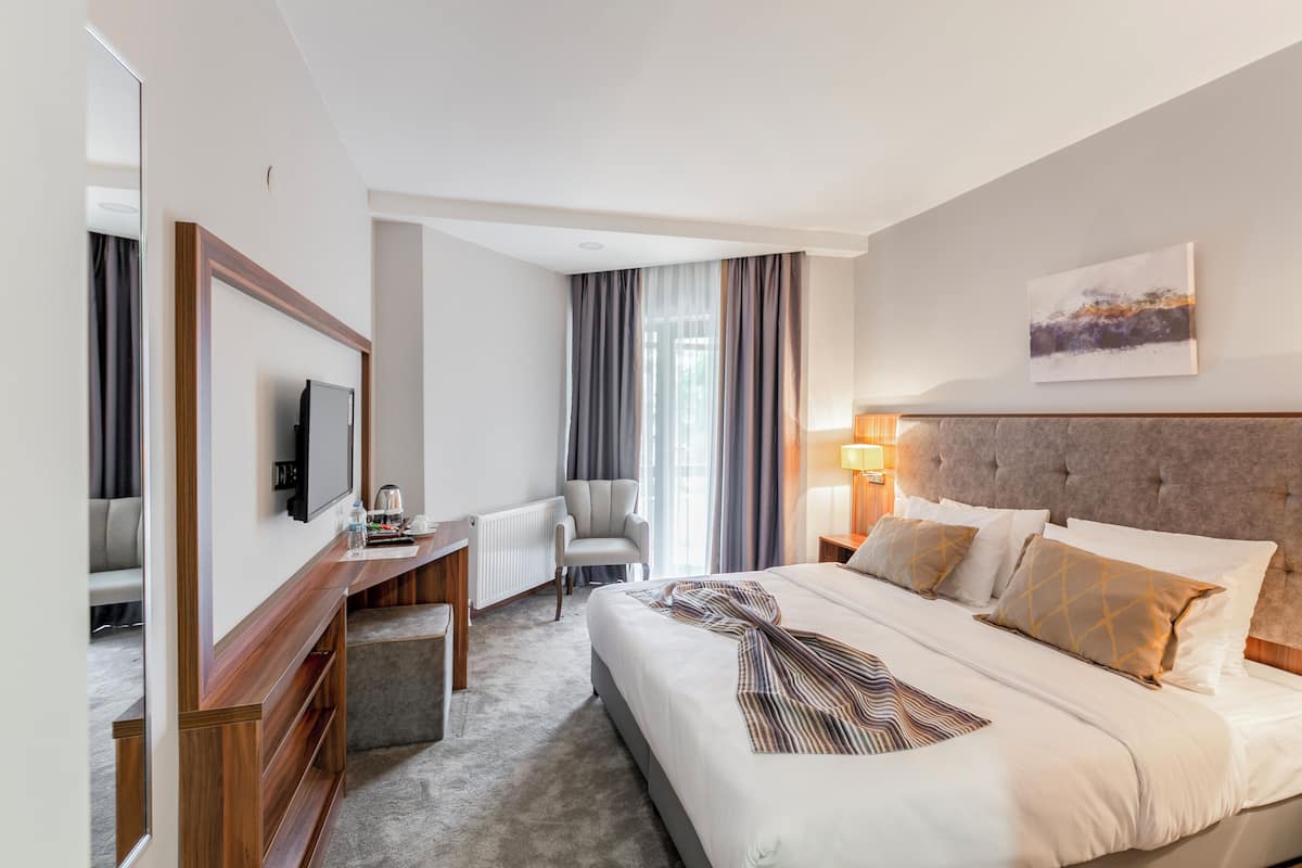 A hotel room with a large bed, a desk with a chair, a television, and a window with curtains.