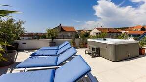 Terraço no telhado com espreguiçadeiras, banheira de hidromassagem e plantas em vasos.