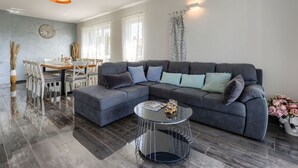 Uma sala moderna com um sofá seccional, uma área de jantar com mesa e cadeiras, e uma janela grande que proporciona luz natural.