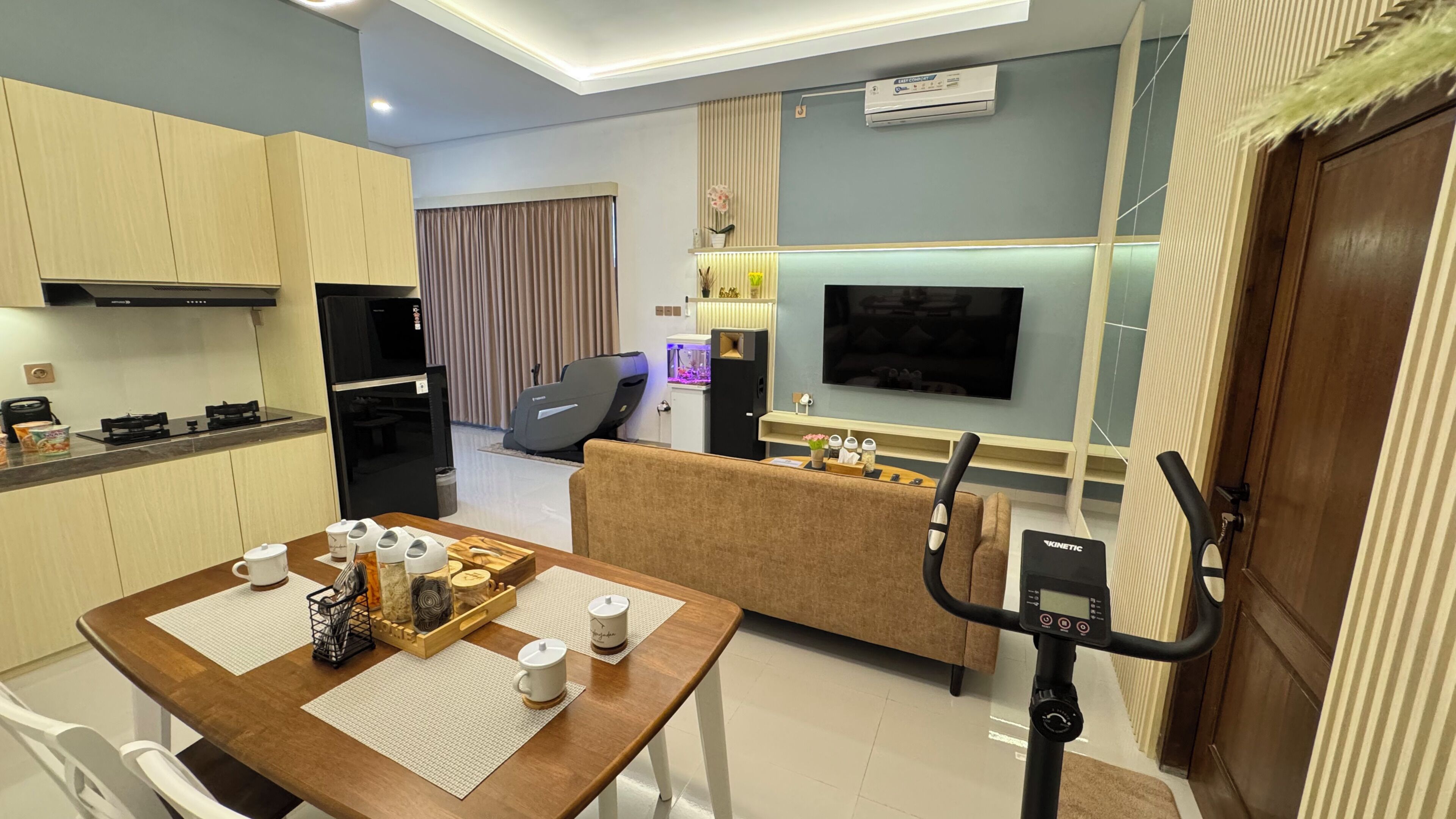 Una sala de estar moderna con un sofá, una mesa de comedor con una bandeja de objetos, un televisor y una cinta de correr.