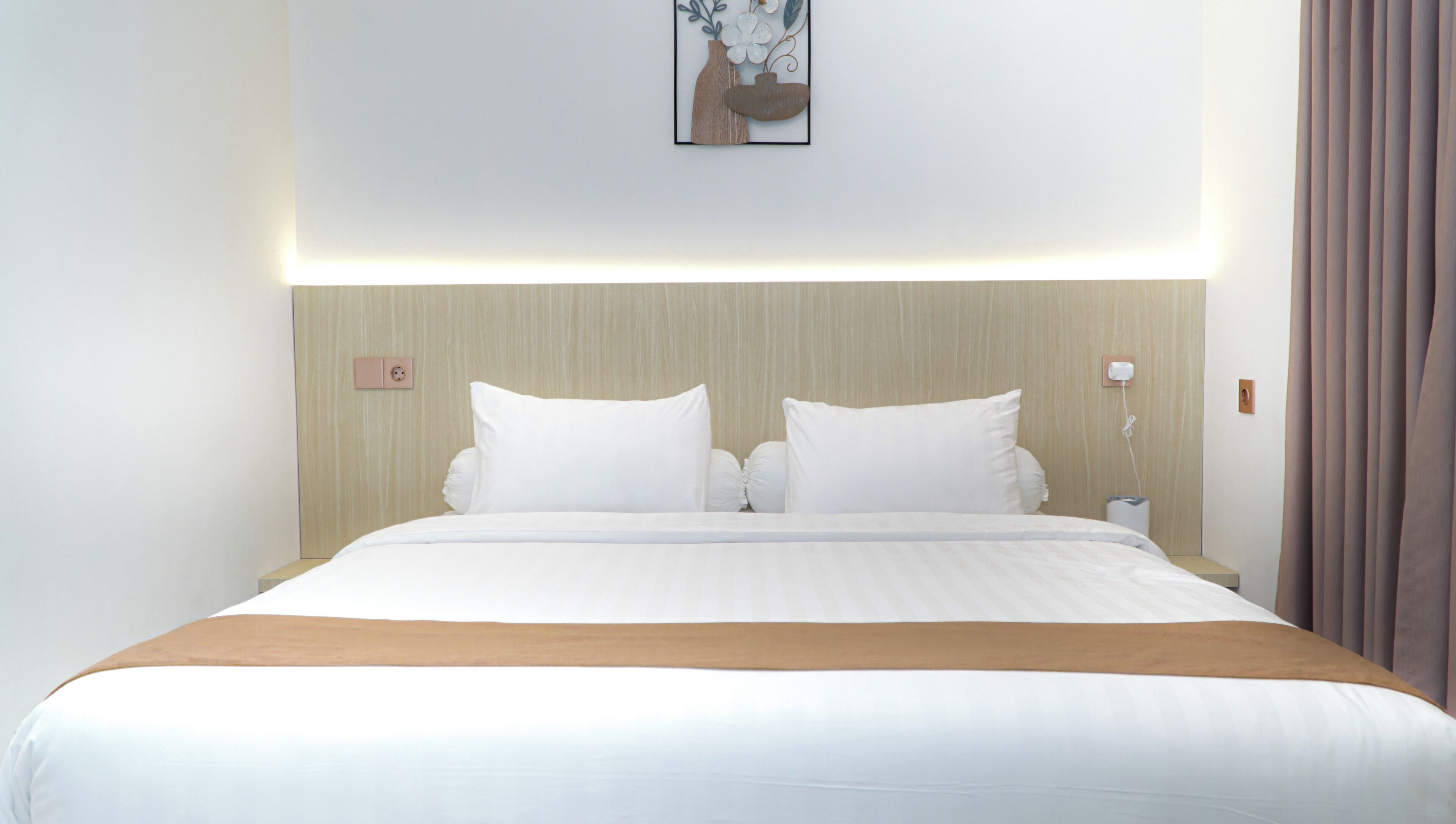 A hotel room with a bed, white bedding, a wooden headboard, a wall-mounted light, and a power outlet.