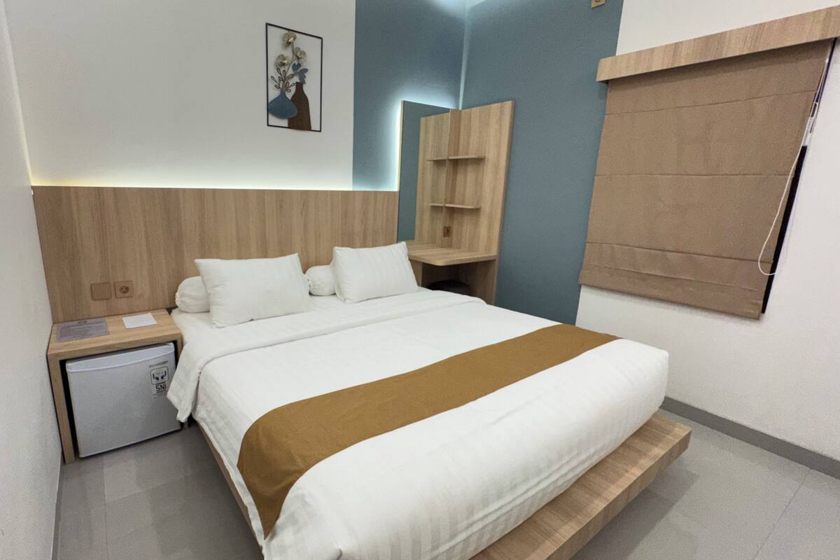Ein Hotelzimmer mit Bett, kleinem Schreibtisch, Spiegel und Fenster mit Jalousien.