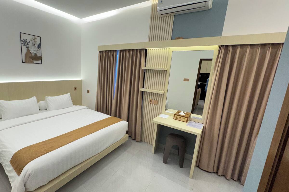 Ein Hotelzimmer mit Bett, Schreibtisch, Spiegel und einem Fenster mit Vorhängen.