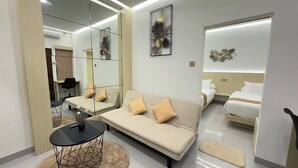 A modern hotel room with a sofa, a small round table, a bed, a mirror, and decorative wall art. - D' Mangkuyudan Luxury Guest House (Yogyakarta)
