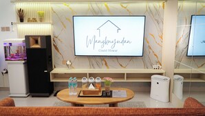 A modern guest room with a large TV displaying 'Mangkokjuan Guest House,' a small aquarium, a water dispenser, and a wooden table with amenities. - D' Mangkuyudan Luxury Guest House (Yogyakarta)