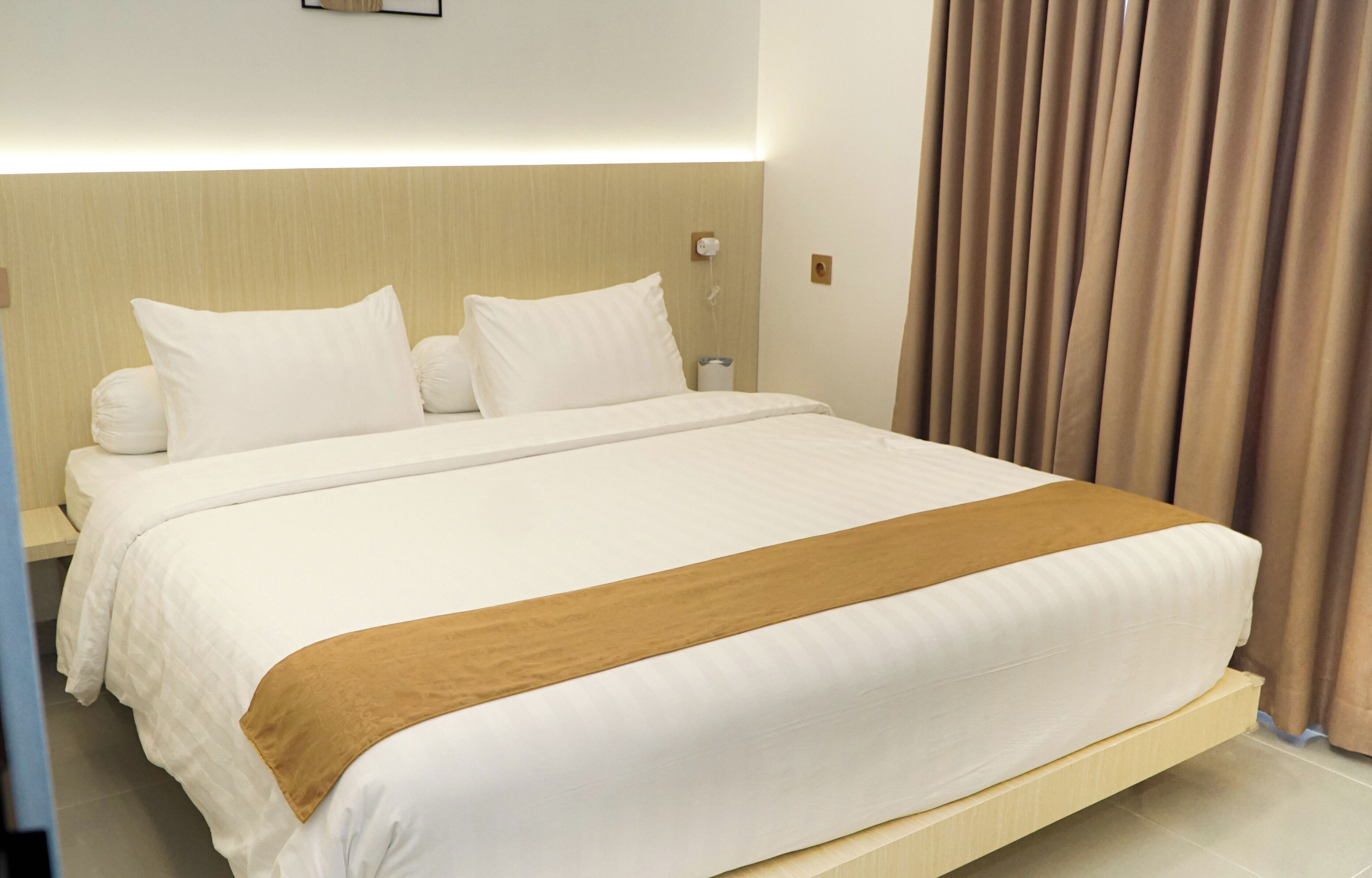 Ein Hotelzimmer mit einem großen Bett, einem Nachttisch, einer Lampe und einem Vorhang.